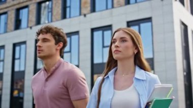 Başarılı erkek kadın modern şehir binasının yakınında birlikte yürüyor. İki kendine güvenen meslektaşı ellerinde defterlerle şehir merkezinde geziniyor. Gülümseyen işadamı kamerayı işaret ederek çalışmaya devam ediyor.