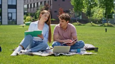 Yeşil üniversite kampüsü çimlerinde oturan güler yüzlü çift doğada öğreniyor. İki genç öğrenci dizüstü bilgisayar ve güneşli park çimlerinde not defterleriyle ders çalışıyor. Neşeli arkadaşlar takım çalışmasının tadını çıkarıyorlar..