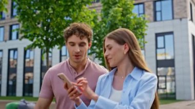 Akıllı telefona bakan gülümseyen bir çift. Güneşli caddede birlikte yürüyorlar. Yakın çekim. Neşeli kadın erkek meslektaşına cep telefonunun komik içeriğini gösteriyor. Şehir binası yakınlarında gezen dost canlısı iş arkadaşları.