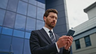 Yatırımcı, modern cam binanın yakınında duran akıllı telefon mesajına seviniyor. Şehir merkezindeki cep telefonundan harika haberler okuyan mutlu iş adamı. Gülümseyen yönetici maddi gelirinden memnun.