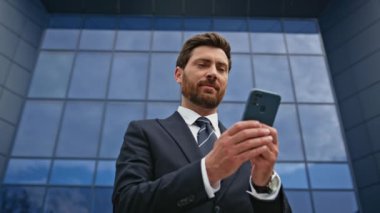 Sokakta cep telefonu bilgilerini okuyan kendine güvenen bir girişimci. Cam ofis binasının yanında akıllı telefon kullanan takım elbiseli profesyonel bir yönetici. Gülümseyen yönetici dışarıda cep telefonu mesajını okuyor.