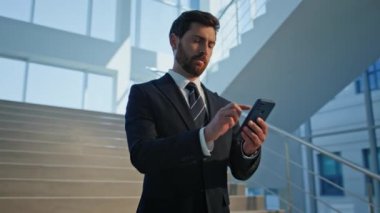Modern ofis binasının içinde merdivenlerde akıllı telefon kullanan bir iş adamı. Takım elbiseli güveni tam bir işletmeci, merdivenlerde duran mobil cihazlara odaklanmış durumda. Zarif patron akıllı telefonu kapalı mekanda mesaj atıyor..