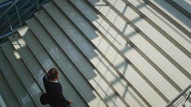 Kendine güvenen yönetici merdivenleri günışığıyla aydınlatan modern ofis. Takım elbiseli azimli bir işadamı evrak çantasıyla merdivenlerden yukarı çıkıyor. Zengin adam buluşmaya koşuyor, el gözetimi yapıyor..