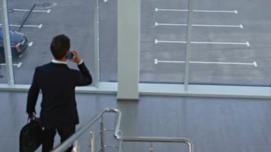 Yürüyen yönetici cep telefonundan bahsediyor iş görüşmesinde evrak çantasıyla acele ediyor. Kendine güvenen iş adamı akıllı telefonu arıyor, modern ofise iniyor. Zarif yönetici konuşan telefonu kontrol ediyor..
