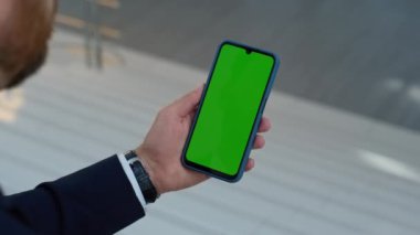 Yönetici elleri ofiste sosyal medya içeriğini izlerken kroma tuşlu cep telefonunu dinliyor. Kimliği belirsiz iş adamı yeşil ekran cep telefonu kullanıyor. Zarif adam internetten akıllı telefondan alışveriş yapıyor..