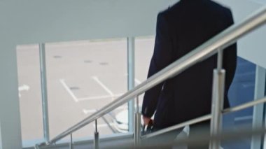 İş adamı elinde evrak çantasıyla ofis merdivenlerinden iniyor. Modern binaların aşağısında yürüyen zarif bir yönetici. Kendine güvenen girişimci merdivenlerden aşağı iniyor..