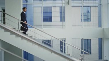 Şirket patronu şık bir takım elbiseyle aşağıya iniyor. Kendine güvenen işadamı merdivenlerden aşağı inerken çantasıyla modern bir bina taşıyor. Şirket lideri merdivenlerden iniyor. Ofisin içini kontrol ediyor..