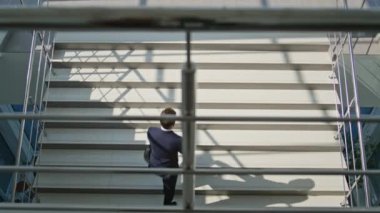 Modern ofis binasında kendine güvenen profesyonel merdivenler. Takım elbiseli şık bir işadamı elinde siyah bir çantayla merdivene tırmanıyor. Üst katta iş görüşmesi için acele eden meşgul bir erkek müdür var.