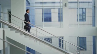 İş sahibi iş gününden sonra aceleyle merdivenlerden iniyor. Başarılı bir iş adamı modern ofis binasına gidiyor. Siyah evrak çantası taşıyan özgüvenli girişimci merdivenlerden iniyor..