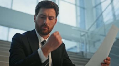 Düşünceli girişimci ofis merdivenlerinde oturarak anlaşma okuyor. Sakallı işadamı, merdivenlerdeki mali raporları analiz ederken gülümsüyor. İş belgelerini tutan mutlu adam başarıyı hissediyor