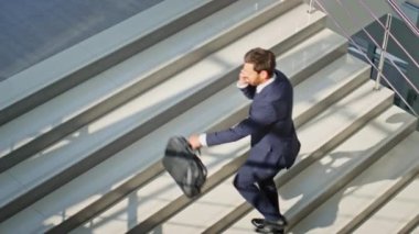 Motive olmuş iş adamı, akıllı telefondan parlak ofis merdivenlerini çıkarken arıyor. Kendine güveni tam bir yönetici, cep telefonunun evrak çantasıyla yukarı çıktığını söylüyor. Sakallı yönetici sabah iş yerinde telefonla konuşuyor..