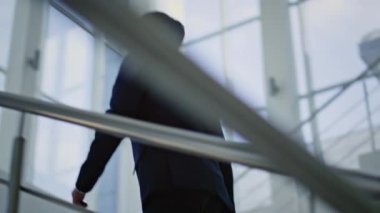 Üst kattaki ışıklı binada zarif bir takım elbise içinde koşmakla meşgul. Kendine güvenen işadamı modern ofis odasındaki cam merdivenlere tırmanıyor. Başarılı girişimci, parlak iç mekanının içine doğru tırmanıyor..