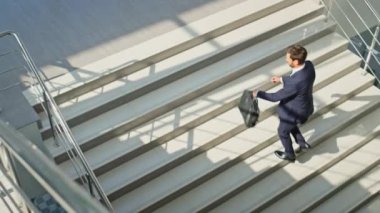 Zengin adam merdivenlere tırmanıyor modern bina evrak çantası taşıyor. Şık takım elbiseli azimli bir işadamı, güneşli merdivenlerden yukarı çıkıyor. Sakallı girişimci iş görüşmesi için acele üst kata çıkıyor..