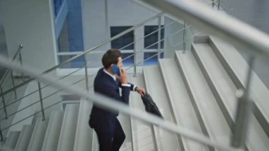 Sakallı yönetici cep telefonunu arıyor. Üst katta modern ışık binasında yürüyor. İş adamı cep telefonuyla merdivene tırmanmaktan evrak çantasıyla bahsediyor. Zengin yöneticilerin iş görüşmesi devam ediyor..