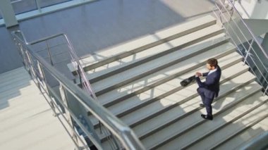 İşletme müdürü ofis içi merdivenlere tırmanıyor. Sakallı işadamı evrak çantası taşıyor ve aceleyle işe gidiyor. Enerjik profesyonel üst kata çıkıyor şık bir takım elbiseyle güneşli bina..