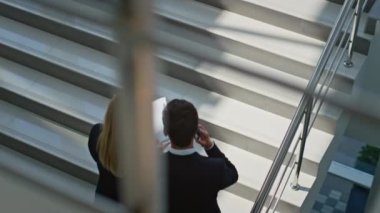 İş çifti merdivenlerden çıkıp belgeleri tartışıyor. Başarılı bir iş adamı üst katta zarif bir iş kadınıyla cep telefonunu arıyor. İki şirket ortağı ellerinde kağıtlarla konuşuyor..