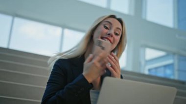 Neşeli iş kadını cep telefonuyla sohbet ediyor ofis merdivenlerinde dizüstü bilgisayarla çalışıyor. Gülümseyen kadın yönetici cep telefonunun elinde belgeler olduğunu söylüyor. Mutlu kadın yöneticiler akıllı telefon konuşmalarının keyfini çıkarın..