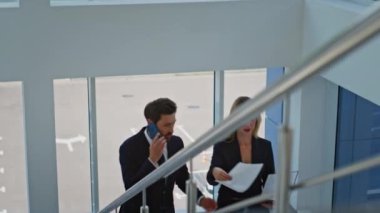 İş kadını üst katta modern ofis binasında birlikte yürüyorlar. Girişimci, sekreterle cep telefonundan belgeleri inceliyor. İş projesinde işbirliği yapan iki meslektaş.