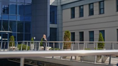 Modern cam ofis binasının yakınında akıllı telefonla yürüyen zarif bir iş kadını. Takım elbiseli sarışın yönetici dışarıda cep telefonuyla konuşuyor. Sokakta cep telefonuyla konuşan kendinden emin bir şirket kadını..