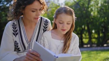 Kadın ebeveyn kızı kitap okuyor. Doğaya yakın oturuyor. Hafta sonunu yaz parkında dikkatle dinleyen sevimli küçük kız. Gülümseyen anne çocuk birlikte dinleniyor. Mutlu aile ilişkileri 
