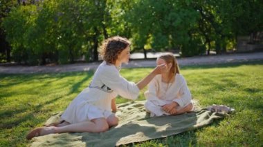 Mutlu anne kızı, aile pikniği battaniyesini çimlere serer. Neşeli anne yaz çimlerinde tatlı sarışın kızı okşuyor. Neşeli haberleşen kadın ebeveyn ve çocuk hafta sonu güneşli.