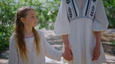 Anne, küçük kızını güzel yeşil parkta el ele gezdiriyor. Gülümseyen küçük kız anne görünümlü aile hafta sonu eğleniyor. Sevimli, güzel bir çocuk kadın kolunu tutuyor. Boş zaman konsepti 