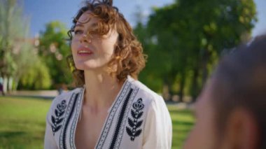 Çimlerin üzerinde oturan gülümseyen kadın parkta küçük kızı yakından dinliyor. Sakin anne güneşli doğanın tadını çıkarıyor. Çekici anne aile pikniğinde küçük kızla iletişim kuruyor. Mutlu ebeveyn çocuk konsepti