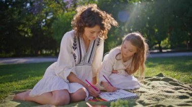 Sunny Meadow 'da piknik yapan kadın çocuk. Mutlu anne, tatlı kız battaniyede gevşeyerek konuşuyor. Küçük kız güzel yeşil çimen doğası üzerine albüm kağıdı boyuyor. Aile hafta sonu konsepti