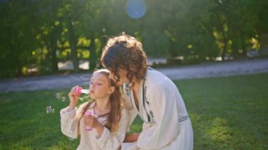 Mutlu bir aile, güneşli parkta yeşil çimlerde oturup sabun köpüğü üflüyor. Çekici anne hafta sonları tatlı kızıyla vakit geçirmekten hoşlanır. Anne ve çocuk arasındaki duygusal bağlar 