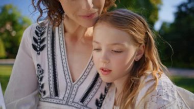 Küçük kız, anne için parkta peri masalı okuyor. Kadın ebeveyn ve küçük çocuk yaz bahçesinde kitap okuyorlar. Önemseyen anne-kız yakınlaşması aile hafta sonu yaşam tarzı 