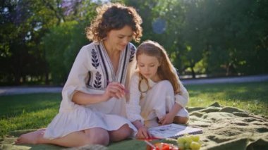Güneşli yeşil çimlerde piknik yapan anne kız. Kaygısız bir kadın açık havada konuşan bir kızla konuşuyor. Rahatlamış mutlu aile hafta sonu doğasının tadını çıkarır. Annelik ve ilişkiler kavramı