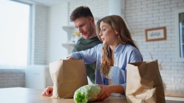 Alışveriş masasını koyan bir çift, marketten yakın çekim için geldiler. Gülümseyen aile, ev mutfağında eko-kağıt paketleri açıyor. Mutlu eşler yemek pişirmek için tezgahta yemek sıralıyorlar. 