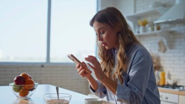 Ev hanımı akıllı telefonları kaydırıyor ve mutfaktaki haberleri yakından takip ediyor. Hafta sonları rahat gülümseyen kadın cep telefonu ekranına bakıyor. Tasasız ev hanımı elinde cep telefonuyla tek başına seviniyor.