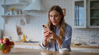 Ev mutfağında cep telefonuyla mesajlaşan kız. Gülümseyen çekici ev hanımı dairede akıllı telefon uygulaması ile online sipariş veriyor. Cep telefonu ekranlı mutlu kadın internette sörf yapıyor. 