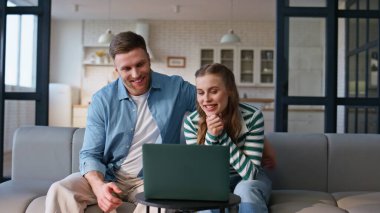 Oturma odasında dinlenirken dizüstü bilgisayarla sanal görüşme yapan ruh eşleri. Neşeli aile çifti evlerinde bilgisayar kameralarıyla çevrimiçi sohbetin tadını çıkarıyor. Gülen çift video çağrısı 