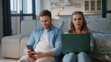 Hafta sonu sabahları evde aletlerle oturan çiftler. Dizüstü bilgisayarda çalışan rahat bir kız arkadaş. Kanepeye yaslanmış akıllı telefondan sosyal medyada gezinen erkek arkadaş. Tasasız aile eğlencesi konsepti 