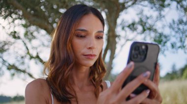 Kırsal modeller akıllı telefonları ağaçların olduğu yere yakın tutuyor. Gülümseyen kadın cep telefonuna temiz hava mesajı atıyor. Rahat kız bahçede modern aletlerle yaz tatilinin tadını çıkarıyor. Teknoloji konsepti 