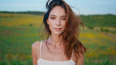 Gülümseyen esmer kamera güzel bir yaz portresinde saçlarıyla oynuyor. Güzel bayan, sarı çiçeklerle doğada poz veren buklelere dokunuyor. Mutlu kız çayırda durup eğleniyor