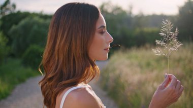 Taşralı kadın kırsal alanda çimlerin üzerinde dinleniyor. Romantik kadın yaz köyünde doğanın tadını çıkarıyor. Kırsal alanda güneş ışığını ısıtan hassas bir model. Nazik bir kız açık havada bitki üflüyor.