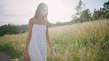 Kırsal kesimde bir kadın elinde sepetle otlakta geziniyor. Dokuma çantası taşıyan mutlu, gülen kadın yaz doğasında yürüyor. Mavi gökyüzü arka planında sıcak havanın tadını çıkaran romantik tasasız model.