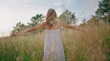Romantik bayan çayıra çıkıyor ve sakin yaz manzarasının tadını çıkarıyor. Mutlu gülümseyen kadın tek başına kameraya bakıyor. Beyaz elbiseli çekici kadın hafta sonları kollarını açıyor.