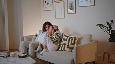 Oturma odasındaki kanepede film seyreden çiftler samimi ve sevgi dolu bir anı paylaşıyorlar. Gülen adam, kadını tutuyor ve birlikte TV gerilim filmi izliyorlar. Rahatlamış eşler aile akşamının tadını çıkarıyor..