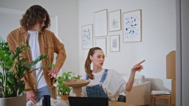 Çift modern evde eşyaları yerleştirirken dekorasyon fikirlerini tartışıyor. Dizüstü bilgisayarı olan bir kadın seramik vazo için kıvırcık adama yer gösteriyor. Eşler yeni evde takım çalışması planlama uzay organizasyonunun keyfini çıkarıyorlar.