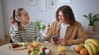 Modern apartman dairesinde eşini üzümle besleyen sevgi dolu bir eş. Gülümseyen kadın aile kahvaltısında adama meyve ikram ediyor. Mutlu adam, kız arkadaşının saçlarını okşuyor, sevgi dolu yuvasını hissediyor..