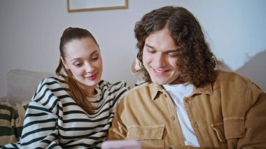 Sevgi dolu eşler birlikte gülümsüyor. Akıllı telefonları yakın çekimde rahat koltuklarda dinleniyorlar. Mutlu eş kulağına fısıldıyor kıvırcık saçlı koca romantik istirahatın tadını çıkarıyor. Rahat çift koltukta cep telefonuna bakıyor..