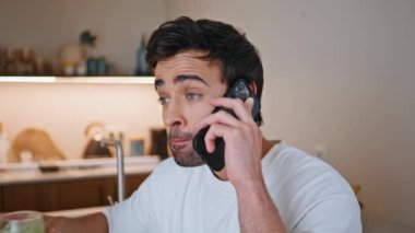 Latin adam akıllı telefondan konuşuyor. Daire mutfağında yeşil smoothie içiyorlar. Yakışıklı adam cep telefonunu arıyor vejetaryen içeceği yudumluyor. Rahatlamış sporcu ev mutfağında cep telefonuyla konuşuyor.
