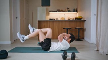 Vücut geliştirme paspasında karın kaslarını çalıştıran aktif bir sporcu. Enerjik genç atlet apartman zemininde el ele tutuşarak bacaklarını kaldırıyor. Her gün karın kaslarını çalıştıran motive bir adam. Sağlıklı erkek vücudu.