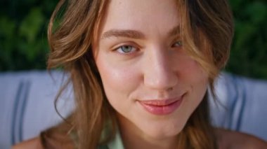 Yakından gülümseyen, yeşil sarmaşık yapraklarıyla çevrili neşeli bir kadın. Rüzgarda dalgalanan saçları düzelten mutlu, güzel bir bayan. Açık havada durgun bir şekilde poz veren şehvetli bir modelin portresi..