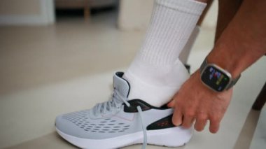 Spor hazırlıklarında spor ayakkabılarını bağlayan erkek elleri kapalı mekanda yakın plan çekimde. Gri ayakkabı giyen tanınmayan sporcu antrenmana hazırlanıyor. Akıllı akıllı kimliği belirsiz aktif bir adam spor salonuna hazırlanıyor..