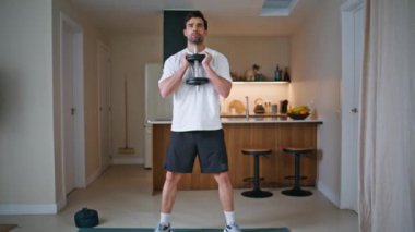 Motive olmuş bir adam aktif ev antrenmanında dambıl kullanıyor. Atletik İspanyol adam apartman mutfağında spor vücut çalıştırıyor. Sağlıklı yaşam pratiği yapan kararlı güçlü bir atlet..